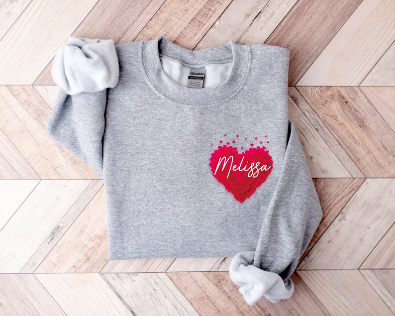 May include: A gray sweatshirt with a red heart made of smaller hearts. The heart has the name "Melissa" written inside it.