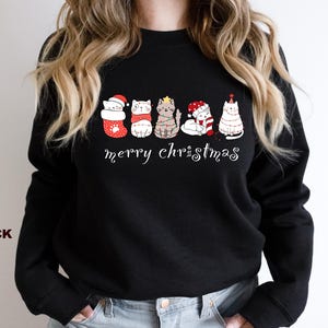 May include: Black sweatshirt with a festive design featuring five cats wearing Christmas hats and ornaments. The text "Merry Christmas" is printed below the cats.