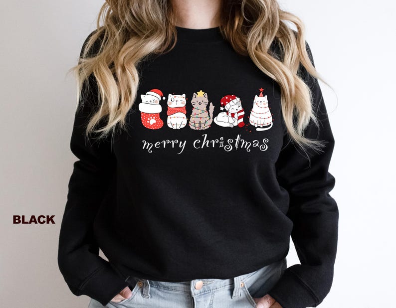 May include: Black sweatshirt with a festive design featuring five cats wearing Christmas hats and ornaments. The text "Merry Christmas" is printed below the cats.