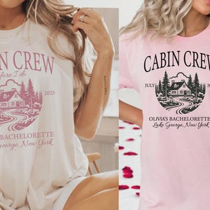 May include: Two short-sleeve t-shirts, one cream and one light pink, each featuring a circular graphic with a cabin, pine trees, and a winding path. The text reads CABIN CREW, before I do, JULY 2025, OLIVIA'S BACHELORETTE, and Lake George, New York.