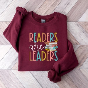 May include: Burgundy sweatshirt with the text "Readers are Leaders" in colorful letters and a stack of colorful books.