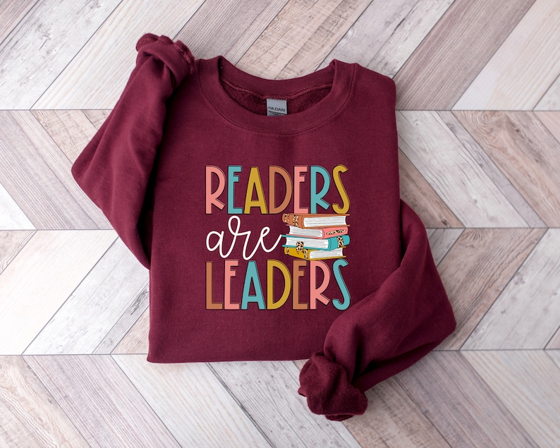 May include: Burgundy sweatshirt with the text "Readers are Leaders" in colorful letters and a stack of colorful books.