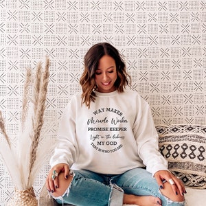 May include: White sweatshirt with a black graphic print that reads "Way Maker, Miracle Worker, Promise Keeper, Light in the darkness, My God That Is Who You Are".