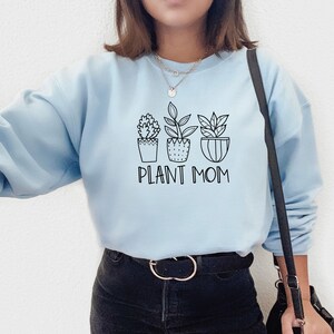 May include: Light blue sweatshirt with a black graphic of three potted plants and the text "Plant Mom".