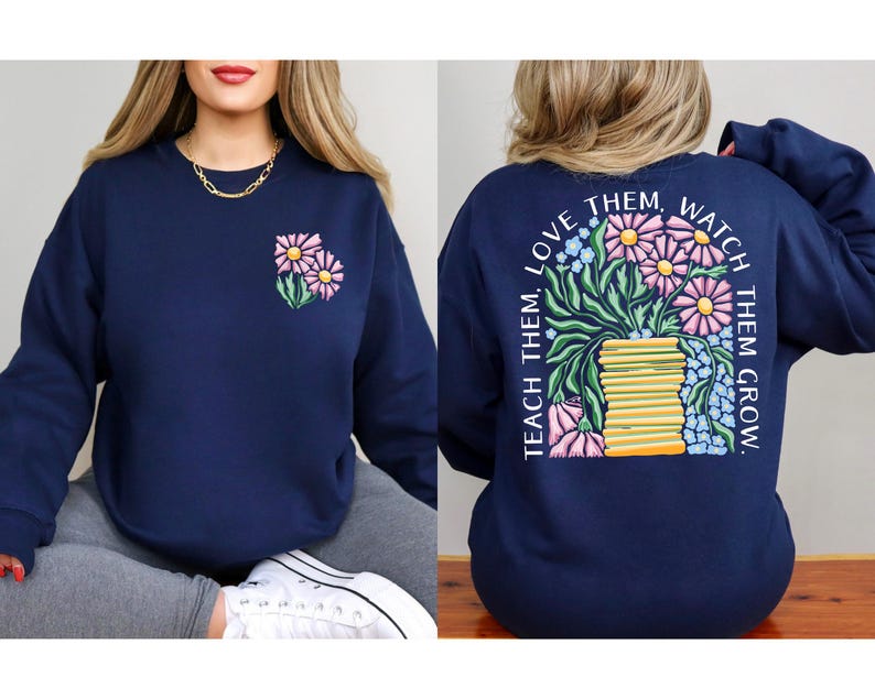 May include: Navy blue sweatshirt with a floral design. The front features a small embroidered bouquet of pink and yellow flowers. The back displays a larger floral arrangement with the text "Teach them, love them, watch them grow."