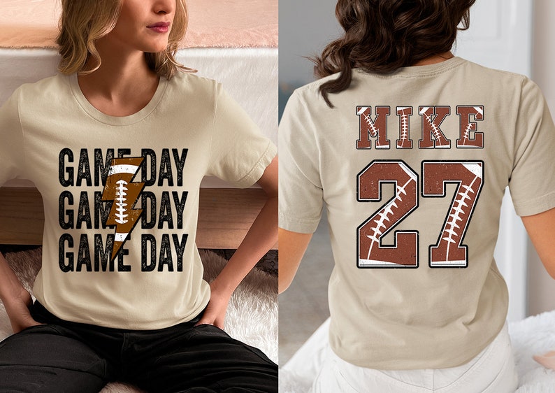 May include: Two beige t-shirts with a football theme. One shirt has the text "GAME DAY" repeated three times with a lightning bolt graphic made of a football. The other shirt has the text "MIKE" and the number "27" with a football graphic.
