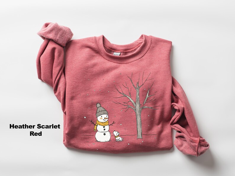 May include: A heather scarlet red sweatshirt featuring a snowman and a dog illustration. The snowman is wearing a yellow scarf and a black hat. The dog is white with a black nose and tail.