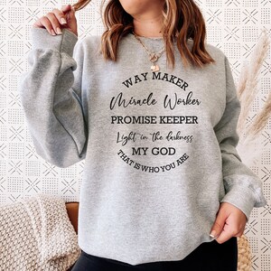 May include: Gray sweatshirt with a black graphic print that reads "Way Maker, Miracle Worker, Promise Keeper, Light in the darkness, My God, That is who you are."