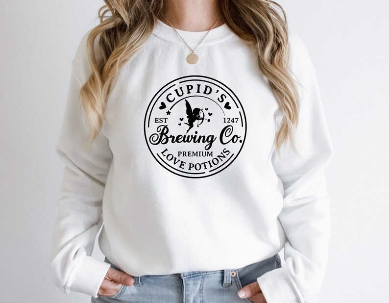 May include: White sweatshirt with a black circular logo that says "Cupid's Brewing Co." with a cupid design and the text "Est 1247 Premium Love Potions".