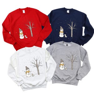 May include: Four different coloured sweatshirts with a snowman and a dog design. The sweatshirts are red, navy blue, white and grey.