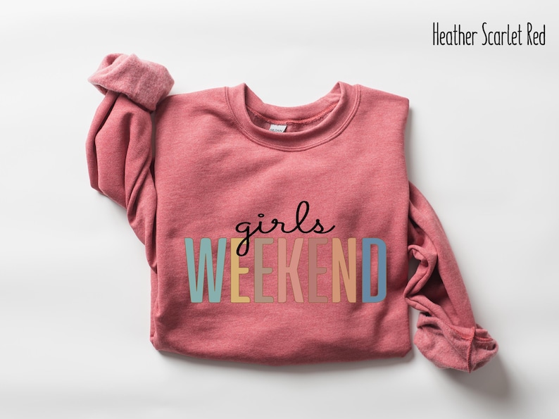 Peut inclure: Un sweat-shirt rouge &eacute;carlate chin&eacute; avec le texte "girls weekend" en couleurs arc-en-ciel.