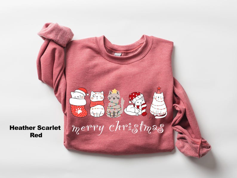 May include: A heather scarlet red sweatshirt with a Christmas design featuring five cats wearing festive attire. The cats are lined up and the text "merry christmas" is printed below them.