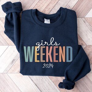 Peut inclure: Un sweat-shirt bleu marine avec le texte "girls weekend 2024" en lettres color&eacute;es.