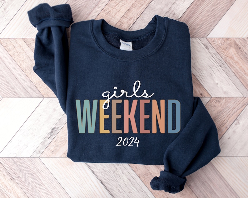 Peut inclure: Un sweat-shirt bleu marine avec le texte "girls weekend 2024" en lettres color&eacute;es.