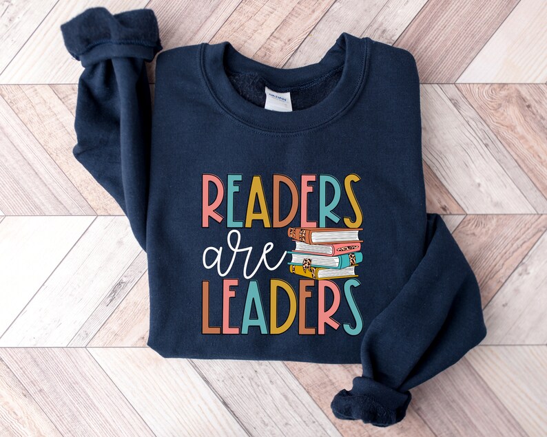 May include: Navy blue sweatshirt with the text "Readers are Leaders" in colorful letters and a stack of books with colorful covers.