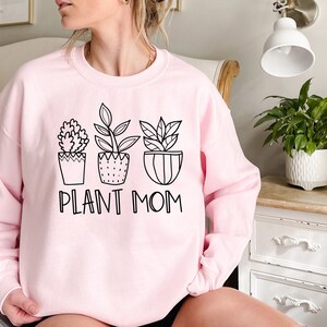 May include: A pink sweatshirt with a black graphic of four potted plants and the text "Plant Mom".