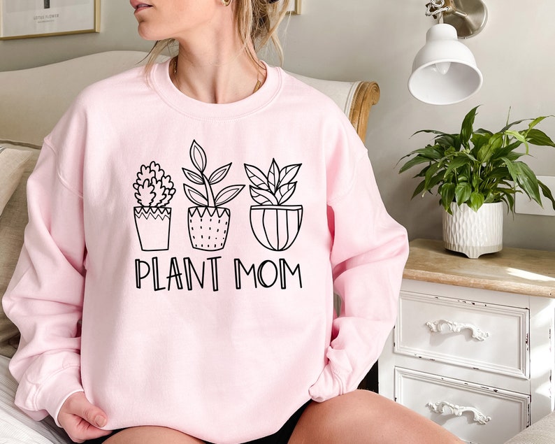 May include: A pink sweatshirt with a black graphic of four potted plants and the text "Plant Mom".