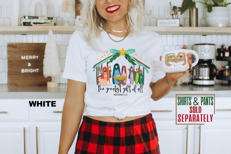 May include: White t-shirt with a colorful illustration of the nativity scene. The text "the greatest gift of all" and "Matthew 1:23" are printed below the illustration.