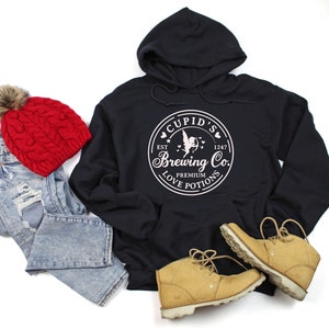 May include: Black hoodie with a white graphic of a cupid with a heart and arrow, and the text "Cupid's Brewing Co. Est. 1247 Premium Love Potions".