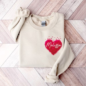 May include: A cream colored sweatshirt with a heart made of pink hearts that says "Melissa" on it.