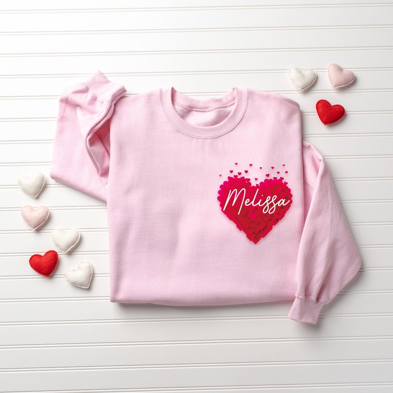 May include: Pink sweatshirt with a large red heart made of smaller hearts. The heart has the name "Melissa" written inside.