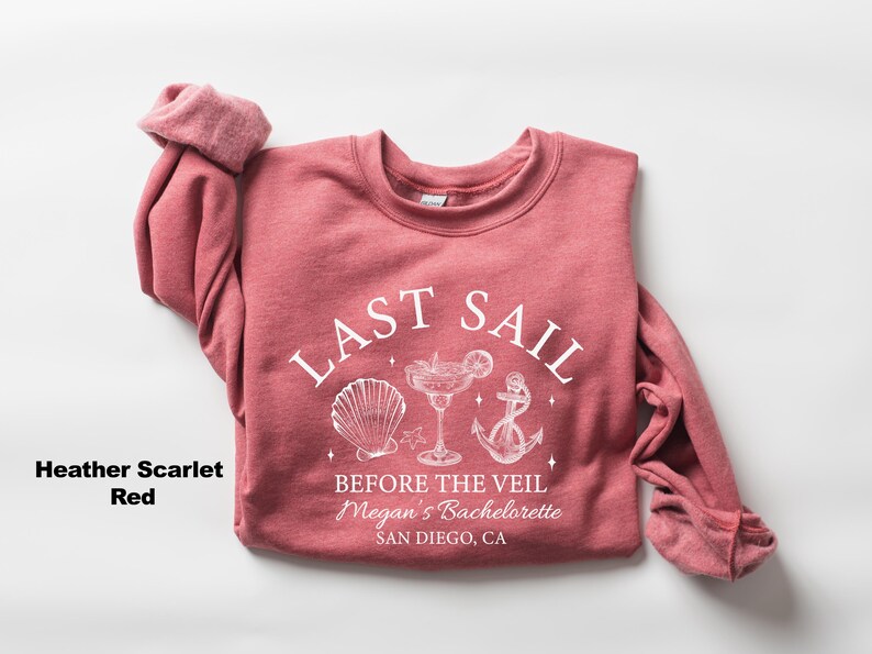 May include: Heather scarlet red sweatshirt with the text "LAST SAIL" above a seashell, cocktail, and anchor graphic. Below the graphic is the text "BEFORE THE VEIL Megan's Bachelorette SAN DIEGO, CA."