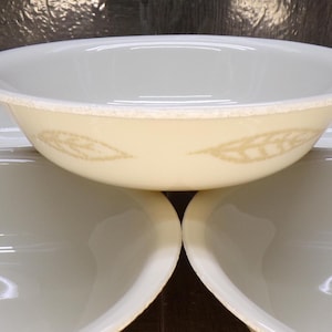 May include: A set of off-white ceramic bowls with a wheat pattern. The bowls have a cream-colored exterior with a wheat design and a white interior. The bowls are stacked, showcasing their shape and design.