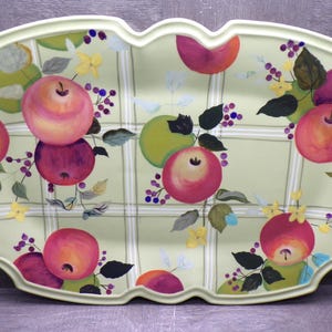 May include: An oval-shaped serving platter with a light green background featuring a white plaid pattern. The surface is decorated with painted red and green apples, dark purple berries, and small yellow flowers arranged across the entire tray.