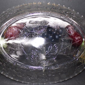 May include: A clear glass oval serving dish with a raised design of grapes, leaves, and berries. The dish has a scalloped edge.