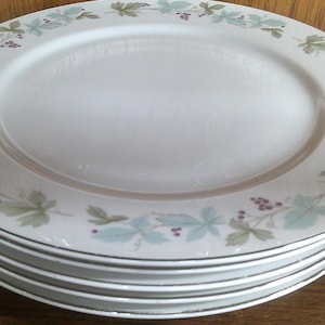 May include: A stack of six white ceramic dinner plates with a green and purple floral design around the rim.