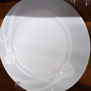 May include: White ceramic dinner plate with a swirl design. The plate has a raised edge and a smooth, glossy finish.
