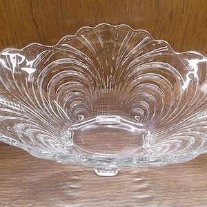 May include: A clear glass bowl with a scalloped edge and a swirl design. The bowl is on a wooden surface.