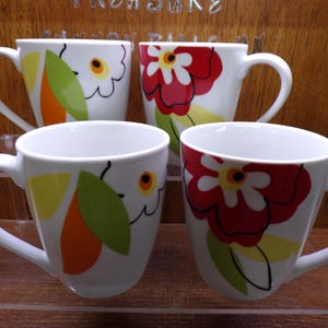 May include: Four white ceramic mugs with large floral designs. Two mugs feature red flowers, while the other two have yellow, orange, and green floral patterns. Each mug has a curved handle and sits on a clear surface.