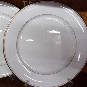 May include: White ceramic plates with a gold rim. The plates have a simple, elegant design, suitable for formal dining. The plates are round and appear to be new.