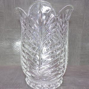 May include: Clear glass vase with a leaf-like pattern. The vase has a flared top and a detailed, textured design. The clear glass allows light to pass through, highlighting the intricate cuts and shapes. A decorative piece for home decor.