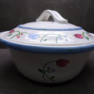 May include: White ceramic casserole dish with a lid, featuring a blue rim and floral design. The dish has a handle on the lid and side handles. The floral pattern includes red tulips and blue flowers.
