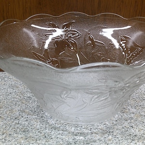 May include: A clear glass serving bowl with a scalloped rim and an etched floral design. The bowl is frosted and has a delicate, feminine look.