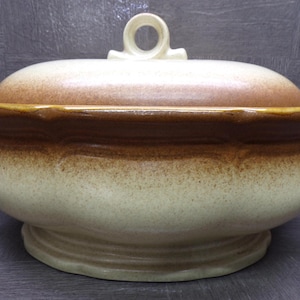 Peut inclure: Une soupière en céramique avec un couvercle. La soupière est de couleur beige moucheté avec une bande marron au milieu et un couvercle marron. Elle a deux poignées et une boucle sur le dessus du couvercle.