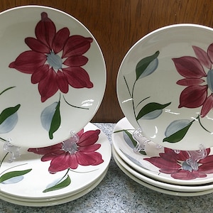 May include: Set of six white ceramic dinner plates with a floral design. The plates feature a large red flower with green leaves and blue accents.