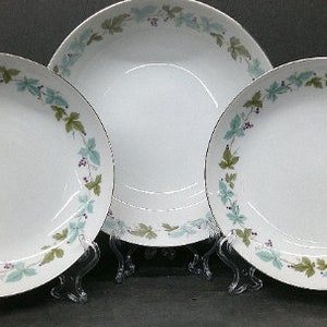May include: Three white ceramic bowls with a green and purple floral design. The bowls are on clear stands.