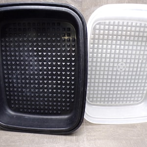 May include: A black plastic rectangular container with a textured interior and a white plastic lid with a grid pattern. The container is open, revealing the interior.