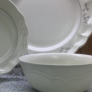 May include: A set of white ceramic dishes with a floral design. The set includes a large dinner plate, a smaller salad plate, and a bowl.