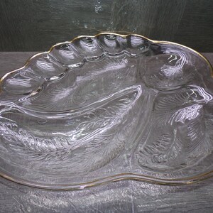 May include: A clear glass serving platter with a scalloped edge and a gold-tone rim. The platter features a molded leaf pattern on the underside, creating a textured surface with multiple divided sections for food arrangement and presentation.
