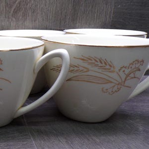 Peut inclure: Un ensemble de tasses à thé en céramique couleur crème avec un motif délicat de tiges de blé dorées sur l'extérieur. Chaque tasse possède une anse incurvée et un fin liseré doré sur le bord supérieur, offrant une finition lisse et arrondie.