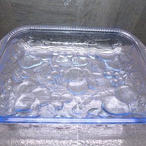 May include: A clear, rectangular glass serving dish with a raised fruit design. The dish has a light blue tint and a beaded edge. The fruit design includes grapes and other fruits. The dish is ideal for serving appetizers or desserts.