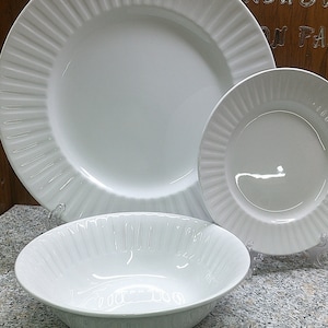May include: A set of three white ceramic plates with a fluted design. The set includes a large dinner plate, a smaller salad plate, and a bowl.