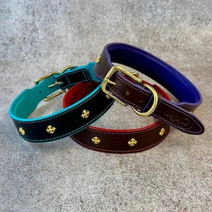 May include: Three leather collars with gold-tone metal buckles and hardware. One collar is black with a turquoise interior, one is dark brown with a red interior, and one is dark brown with a purple interior. Each features small gold cross studs.