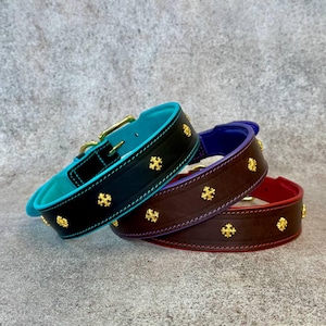 May include: Three leather collars featuring gold-tone cross-shaped studs. The first is black with a turquoise interior, the second is dark brown with a purple interior, and the third is dark brown with a red interior, each with a metal buckle.