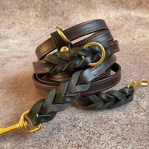 May include: Black leather dog leash with red stitching and a braided design. The leash has a brass clasp and a brass ring.