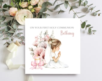 May include: A white card with pink floral illustrations and a girl in a white dress praying. The card says "On your First Holy Communion Bethany".